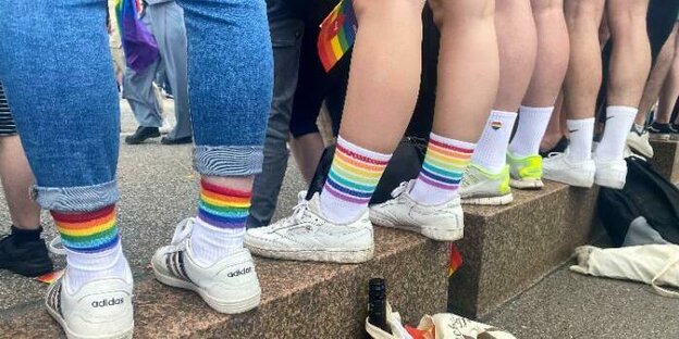 eine Reihe von Beinen, alle tragen weiße Sneaker und regenbogen-farbene Socken