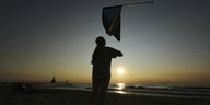 Sonnenuntergang, eine Person am Strand, die eine Flagge einholt