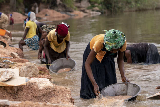 Frauen bücken sich und sieben Wasser in einem schlammigen Fluss in einer Metallschüssel