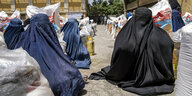 Frauen in blauen und schwarzen Burkas kauern zwischen Lebensmittelsäcken