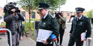 Ein Mann in Polizeiuniform mit Aktenordner geht an der Presse vorbei