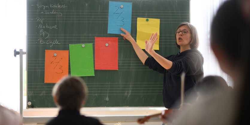 Eine junge Lehrerin steht an der grünen Tafel und erklärt