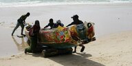 Männer schieben Pirogue am Strand in Senegal