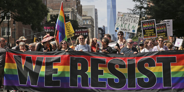 Teilnehmer des Queer-Liberation-Marsches ziehen durch die Stadt. Sie schwenken Fahnen und stehen vor einem Banner mit der Aufschrift "WE RESIST".