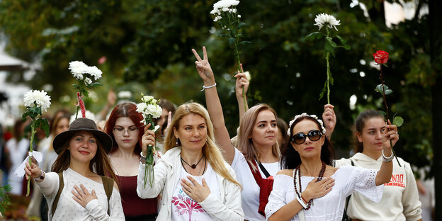 Frauen marschieren in einer Reihe und heben rote und weiße Blumen
