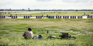 Mensch mit nacktem Oberkörper sitzt auf dem Tempelhofer Feld im Gras