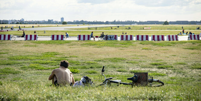 Mensch mit nacktem Oberkörper sitzt auf dem Tempelhofer Feld im Gras