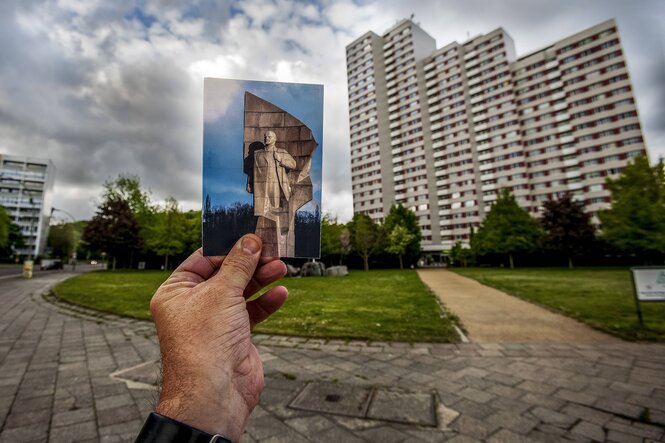 Eine Postkarte mit dem Bild des Lenindenkmals wird an dem Platz in Berlin hochgehalten, an dem das Denkmal bis kurz nach der Wende stand