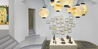 Blick in die Ausstellung von Atsushi Kaga. An der Decke hängen Lampions, auf die gezeichnet wurde, das Wort "End" ist auf einem gezeichneten Marker, wie sie von Wegesrändern bekannt sind, zu lesen. Darunter steht auf einem Sockel eine Gruppe aus Bronzesku
