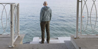 Ein älterer Mann steht am See und blickt auf das Wasser