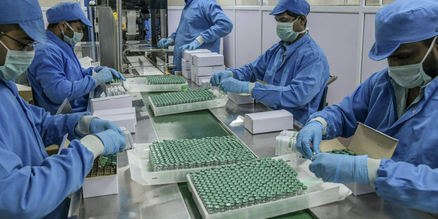 Arbeitende in einer Fabrik verpacken in blauer Schutzkleidung Impfstoffdosen