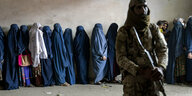 Frauen in Afghanistan stehen Schlange, ein bewaffneter Talibankämpfer überwacht alles.