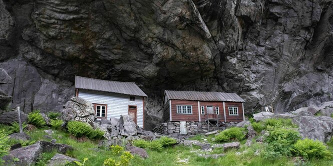 Holzhäuser vor Felsen.