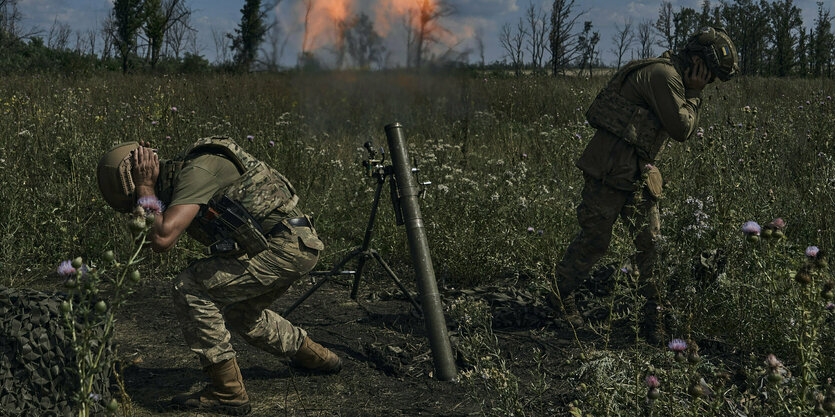 Zwei Soldaten halten sich die Ohren zu, nachdem sie eine Rakete abgeschossen haben, Blumen blühen im Feld