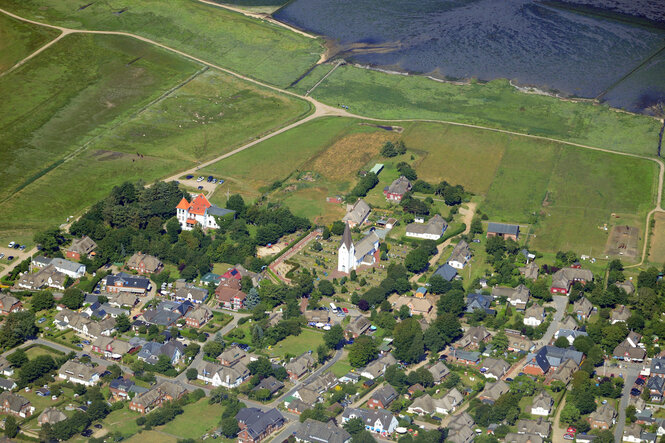 Luftbild: ein kleines Dorf mit Kirche, von Ackern und Meer umgeben