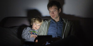 Vater und Kind schauen einen Film auf dem Sofa.