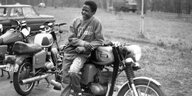ein lachender Schwarzer Jugendlicher lehnt an einem Motorrad