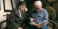 Eine alte Frau und ein alter Mann sitzen nebeneinander und schauen in ein Buch