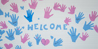 Das Wort "Welcome" umgeben von Handabdrücken auf einer Wand