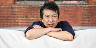 Yi-Wei Keng stützt seine Arme vor einer roten Backsteinwand auf