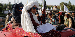 Zwei Jungen mit Turban und Sonnenbrillen sitzen am 15. August in Kabul auf einem roten Wagen mit offenem Verdeck, einer hat ein geschmücktes Gewehr in der Hand