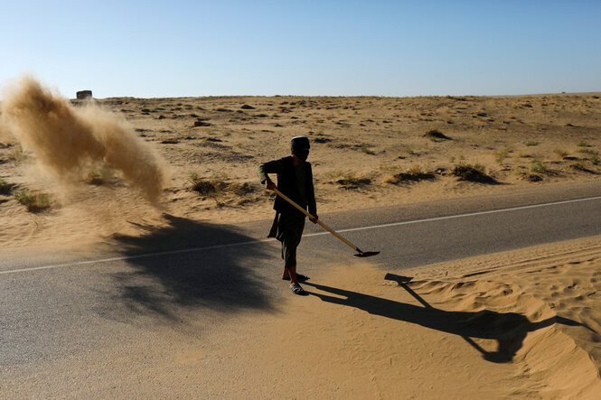 Ein Mann kehrt Sand von einer Straße in einer wüstenartigen Gegend