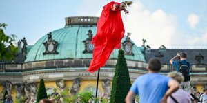Eine Frau im roten Kleid schwebt an einem Stock im Schlossgarten von Schloss Sanssouci