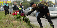 Ein schwarz Uniformierter mit Russlandemblem und Abzeichen der Wagnertruppe legt Blumen ab am Wegrand