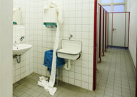 Eine benutzte Handtuchrolle liegt vor dem Handtuchspender in einer Schultoilette auf den Boden