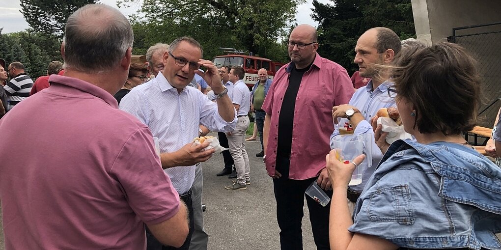 Eine Gruppe von menschen steht beieinander. Sie reden, einer hat eine Bratwurst in der Hand