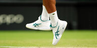 Zu sehen sind die weißen Schuhe und die weißen Socken eines hochspringenden Tennisspielers