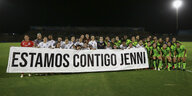 Ein Frauenfußballteam kniet auf dem Rasen. Vor sich hält es ein Banner mit spanischer Aufschrift, die übersetzt lautet: Wir stehen zu Dir, Jenni.