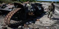 Ein Soldat begutachtet einen zerstörten Panzer auf einer Landstraße