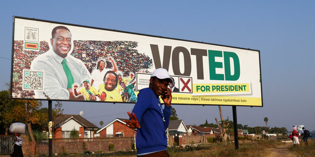 Vor einer Plakatwand mit Werbung für Präsident Mnangagwa telefoniert ein Mann mit dem Handy