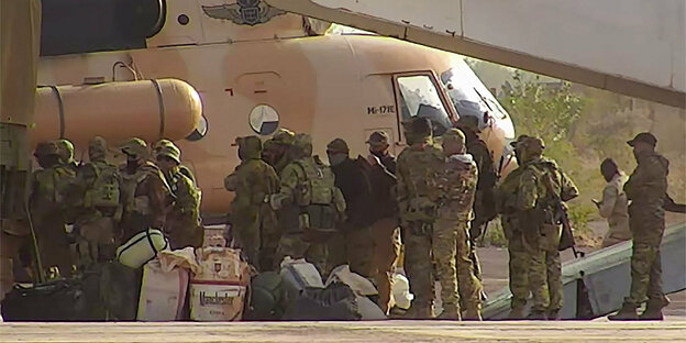 Etwas zwanzig Menschen in militärischer Kleidung stehen bei mehrern Helikoptern