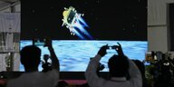 Das Bild zeigt Menschen, die mit ihren Handys die Mondlandung der indischen Mission Chandrayaaan-3 von einer Leinwand abfilmen.