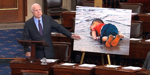 Senator John McCain steht neben einem Bild von Aylan Kurdi, dem toten syrischen Jungen, der ertrunken war