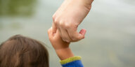 Zu sehen ist die Hand eines Erwachsenen, der eine Kinderhand hält, und der Haarschopf eines kleinen Kindes
