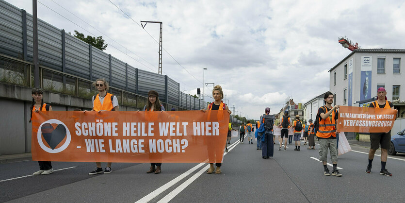 Aktivist*innen der Letzten Generationen laufen mit Transparenten und Warnwesten eine Straße entlang.