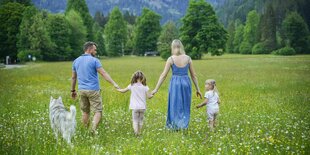 Eine Familie mit Hund und zwei Kindern geht über eine idyllische Wiese