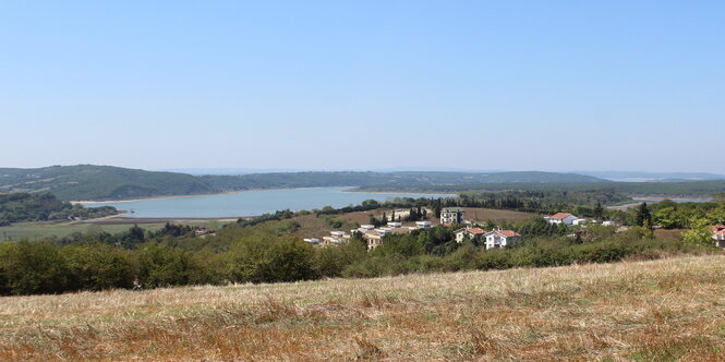 Ein See im Hintergrund, ein Dorf und ein Stoppelfeld