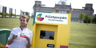 Michael Bohmeyer, Initiator von Mein Grundeinkommen, steht mit einem Geldschein über 1200 Euro ? neben einem Geldautomaten vor dem Bundestag in Berlin