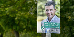 Wahlplakat an einem Baum von Robert Nitz, im Hintergrund stehen Bäume