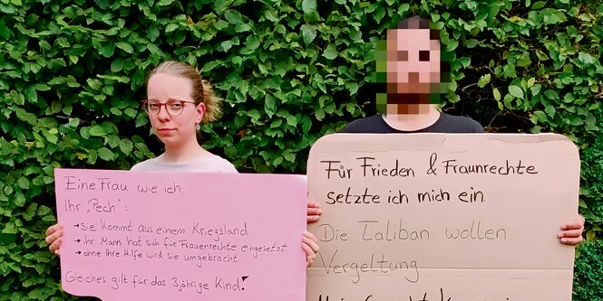 Faheem Majidi und eine Unterstützerin stehen vor einer Hecke und halten Protest-Plakate.