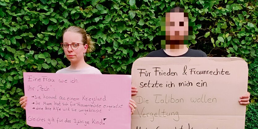 Faheem Majidi und eine Unterstützerin stehen vor einer Hecke und halten Protest-Plakate.