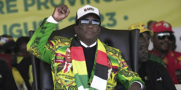 Simbabwes Präsident Emmerson Mnangagwa sitzt in einem bunten Anzug, den Farben Simbabwes mit erhobener Faust in einem Sessel