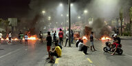 Menschen sitzen auf der Straße vor brennenden Barrikaden