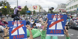 Menschen halten Plakate mit der Aufschrift "Stop A 100" in ihren Händen. Sie liegen auf dem Boden als Teil eines Flashmobs gegen den geplanten Ausbau der Berliner Stadtautobahn A 100 bis zur Frankfurter Allee.