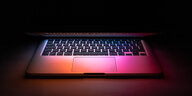 Ein halb geschlossener Laptop in der Dunkelheit mit buntem Monitorlicht