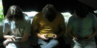 Drei junge Menschen sitzen nebeneinander und blicken auf ihre Handys